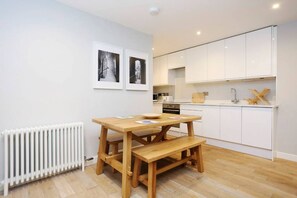 Une cuisine moderne avec des meubles blancs, une table en bois et des bancs, ainsi que deux tableaux encadrés accrochés au mur.