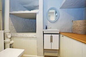 Une salle de bain avec un lavabo blanc, un miroir rond et un plan de toilette en bois.