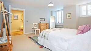 A bedroom with a bed, a dresser, a chair, a ladder, and a door leading to another room.