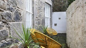 A stone building with a small patio area featuring two wicker chairs and a potted plant.