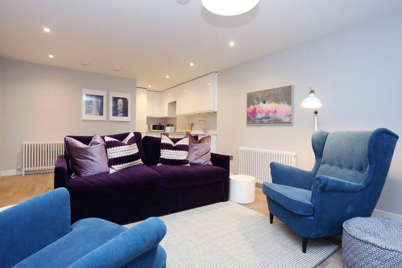 A modern living room with a purple sofa, blue armchairs, and a white rug.