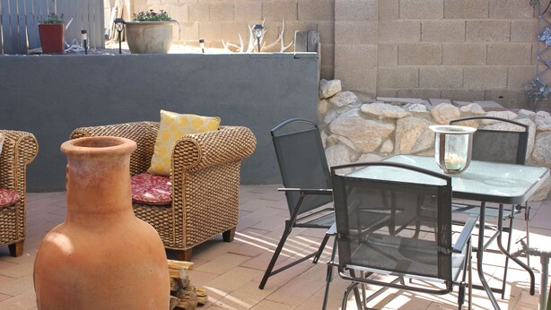 Un patio al aire libre con mobiliario de mimbre, una mesa de vidrio y una gran maceta de terracota.