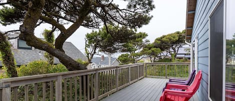 Een houten terras met rode Adirondack-stoelen, een leuning en uitzicht op omliggende bomen en huizen.