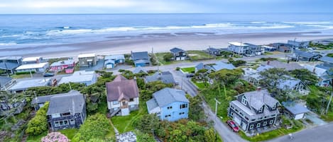An aerial view of a coastal residential area with houses, a beach, and a road.