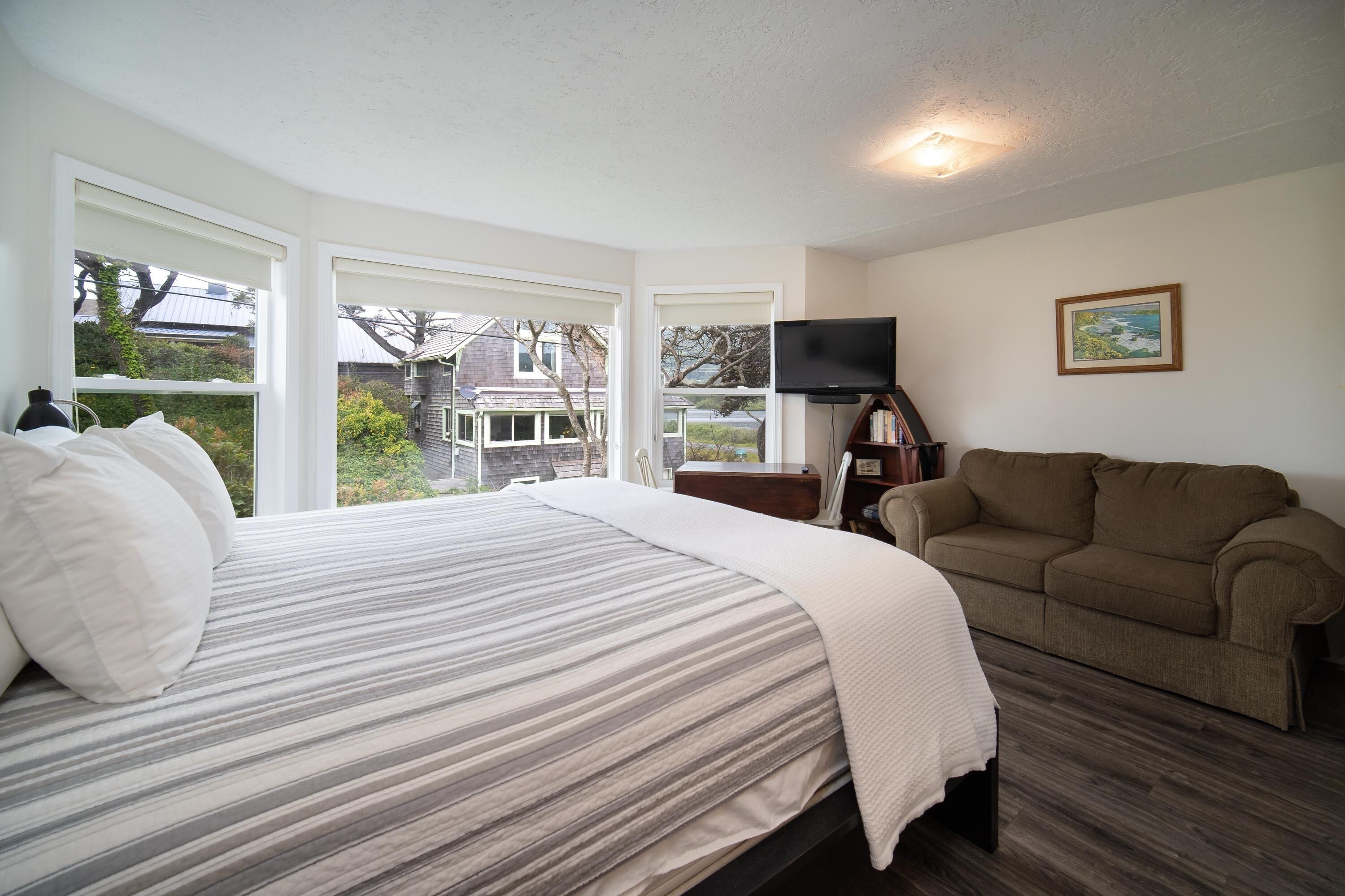 A bedroom with a bed, a television, a couch, and large windows.