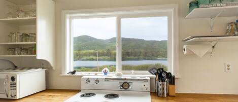 A kitchen with a stove, a microwave, and a window with a view of a lake and hills.