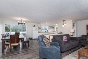 A modern living room with a dining area, a kitchen, and large windows offering a view of a lake.