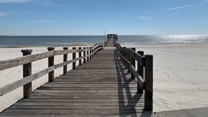 Een houten steiger die naar een strand loopt, met een heldere lucht.