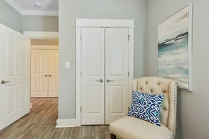 A hallway with a white door, a tufted armchair with a patterned cushion, and a framed artwork on the wall.