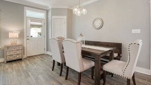 Een eetgedeelte met een houten tafel en vier beklede stoelen met knoopdetails. Een witte bijzettafel met een lamp is zichtbaar.