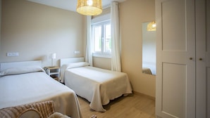 Ein Hotelzimmer mit zwei Betten, einem Korbstuhl, einem Fenster mit Vorhängen und einer Tür.