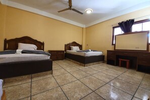 A hotel room with two beds, a desk, a chair, a ceiling fan, and a window with curtains. - Hotel Colonos By Rotamundos  (Cabo San Lucas)
