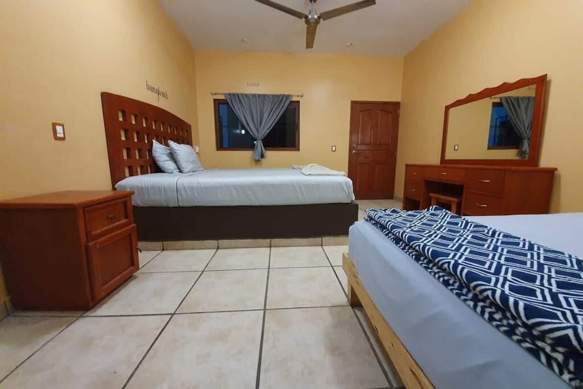 Een slaapkamer met twee bedden, een houten dressoir, een spiegel en een plafondventilator.