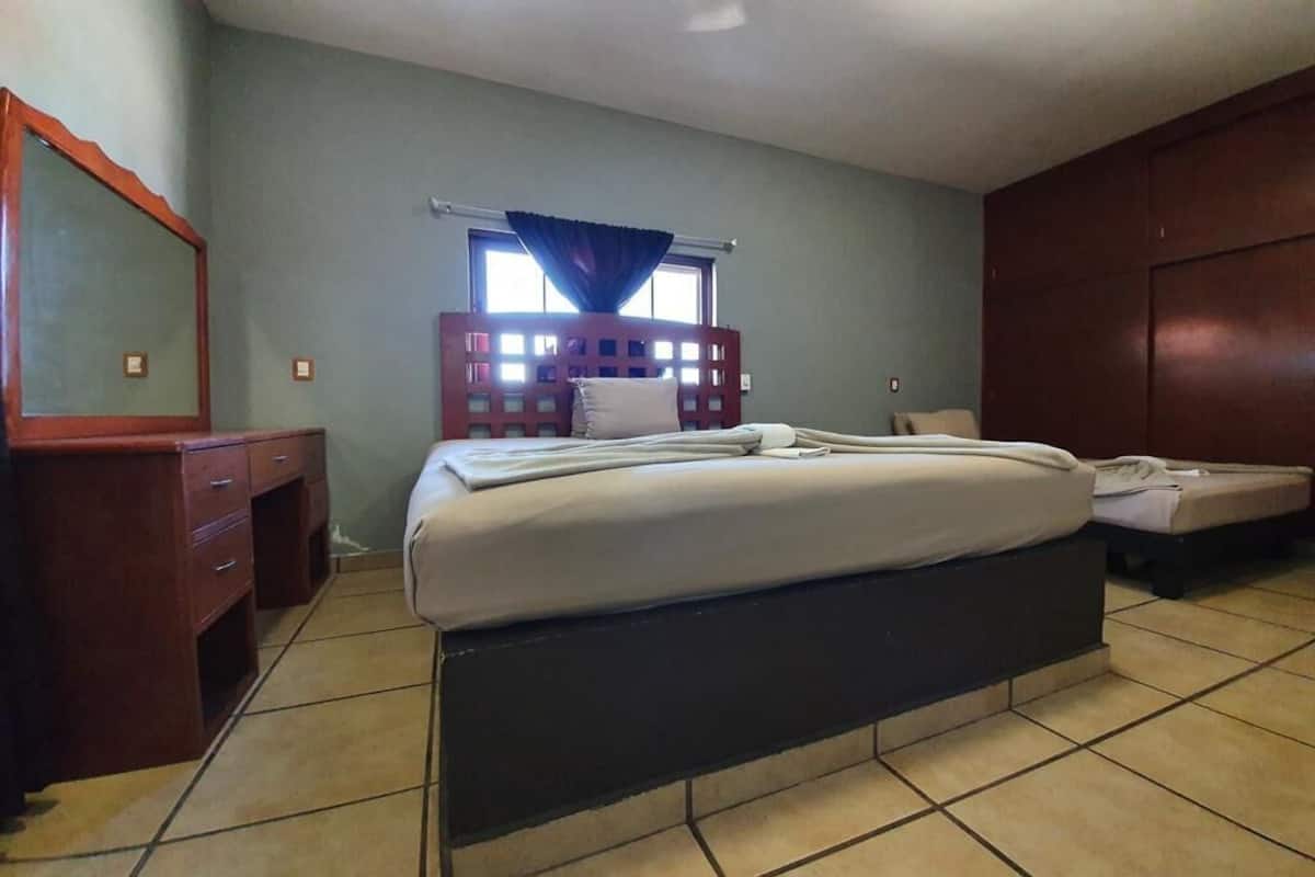 Een slaapkamer met een groot bed, een dressoir, een spiegel en een raam met gordijnen.
