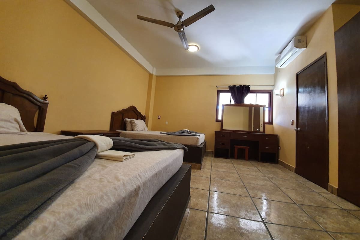 Een slaapkamer met twee bedden, een plafondventilator, een airconditioning, een dressoir, een spiegel en een deur.