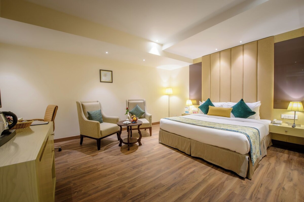 A hotel room with a large bed, two armchairs, a small table, and a desk with a lamp.