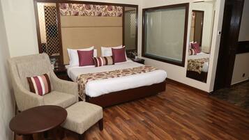 A hotel room with a large bed, a sitting area with a chair and a small table, a large window, and a mirror on the wall.