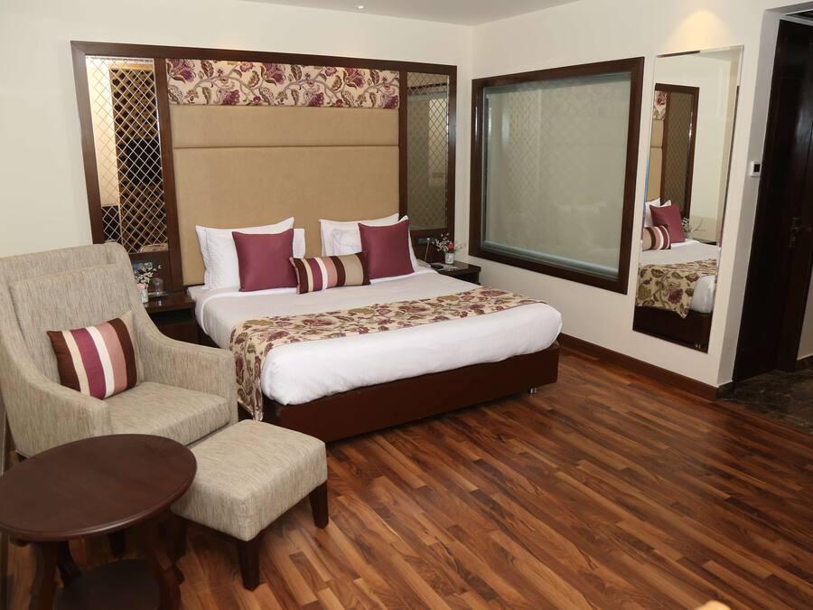 A hotel room with a large bed, a sitting area with a chair and a small table, a large window, and a mirror on the wall.