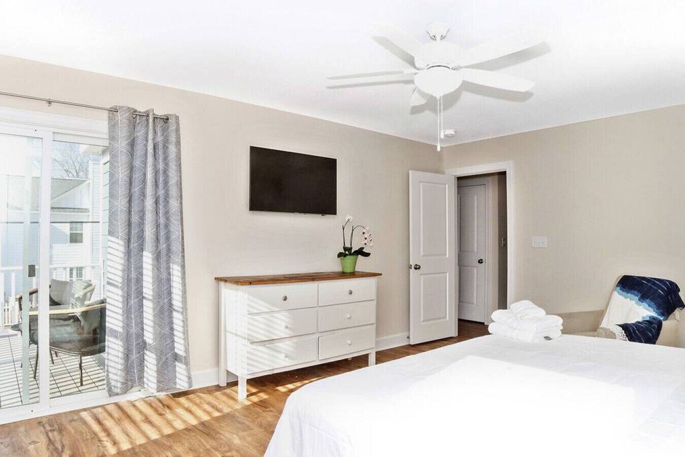 A bedroom with a bed, a dresser, a ceiling fan, a door, and a window with curtains.