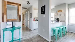 A modern kitchen with a bar area, white cabinets, and teal bar stools. - Sunny Cottage At Byrd Pard In Richmond (Richmond)