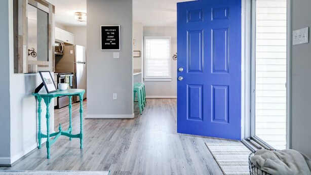 A hallway with a blue door, a framed welcome sign, a teal table, and a bicycle in the background. - Sunny Cottage At Byrd Pard In Richmond (Richmond)