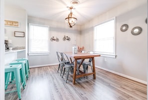 A dining area with a wooden table and chairs, a chandelier, and a window with blinds.