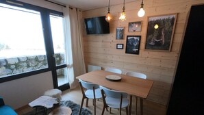 A modern dining area with a wooden table and chairs, a mounted TV, and framed pictures on the wall. - APARTMENT 4/6 people AT THE FOOT OF THE SLOPES (Méribel-Mottaret)