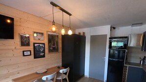 A modern kitchen with wooden cabinetry, a built-in oven, and a refrigerator. There is a dining area with a wooden table and white chairs. - APARTMENT 4/6 people AT THE FOOT OF THE SLOPES (Méribel-Mottaret)
