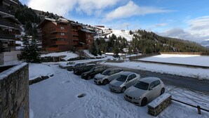 A snow-covered parking lot with several cars, a stone wall, and a building with balconies. - APARTMENT 4/6 people AT THE FOOT OF THE SLOPES (Méribel-Mottaret)