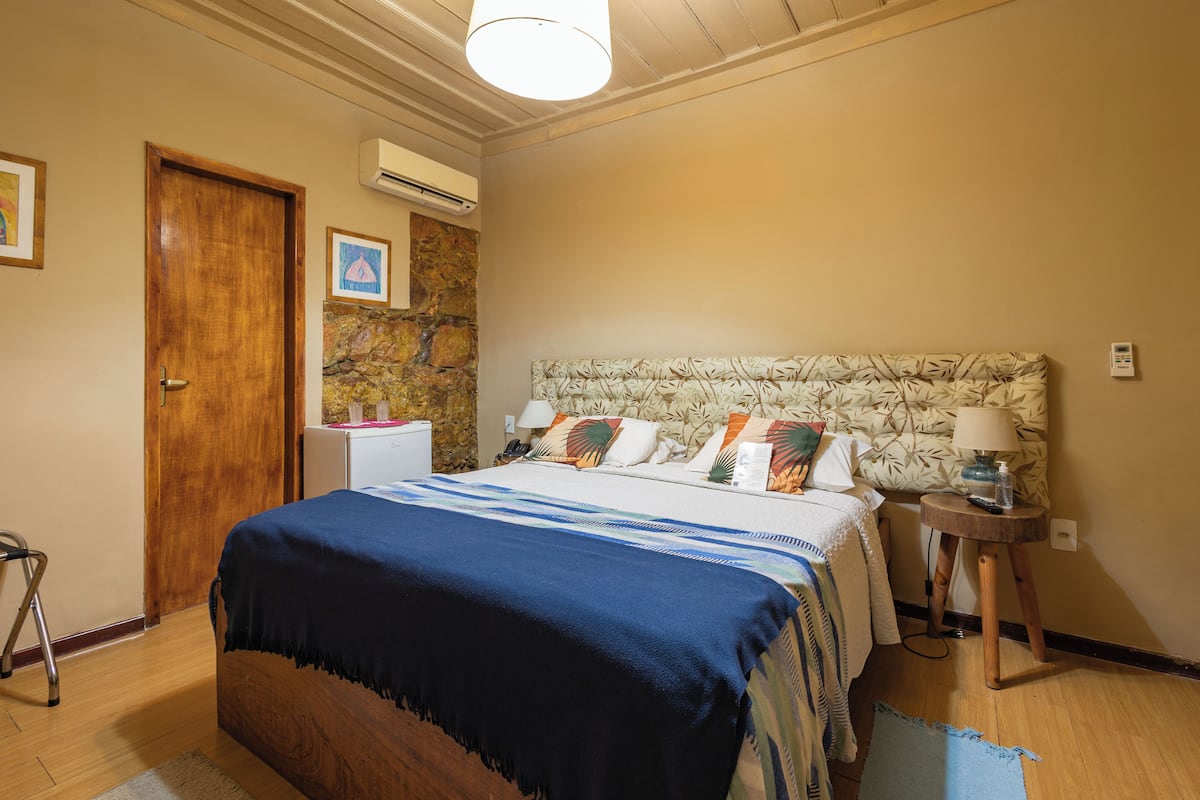 Une chambre à coucher avec un lit en bois, une table de chevet, une lampe, un climatiseur fixé au mur et une porte.