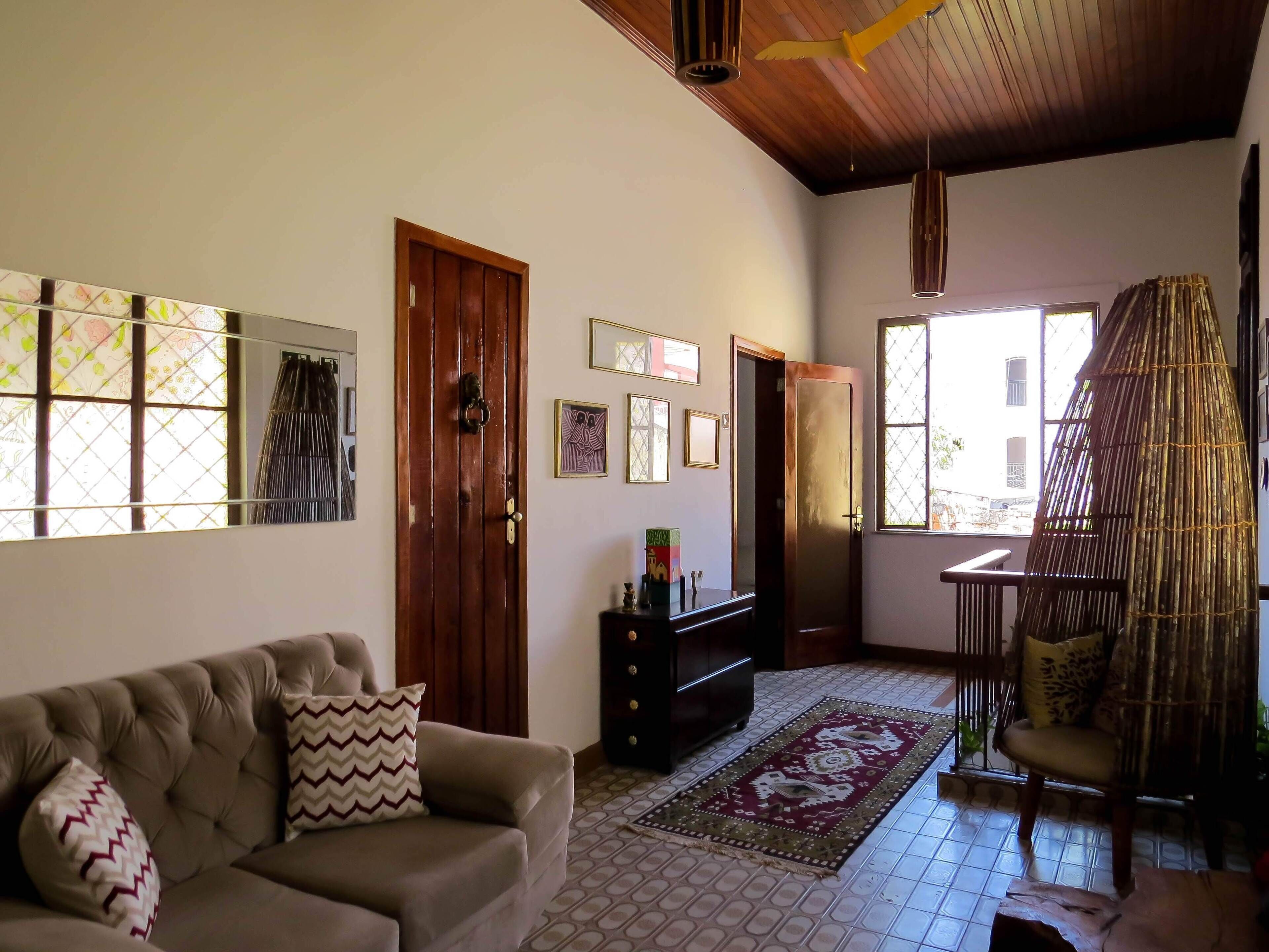A living room with a sofa, a wooden door, a window with a view, and a decorative chair.