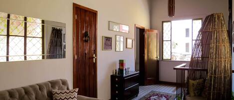 A living room with a sofa, a wooden door, a window with a view, and a decorative chair.