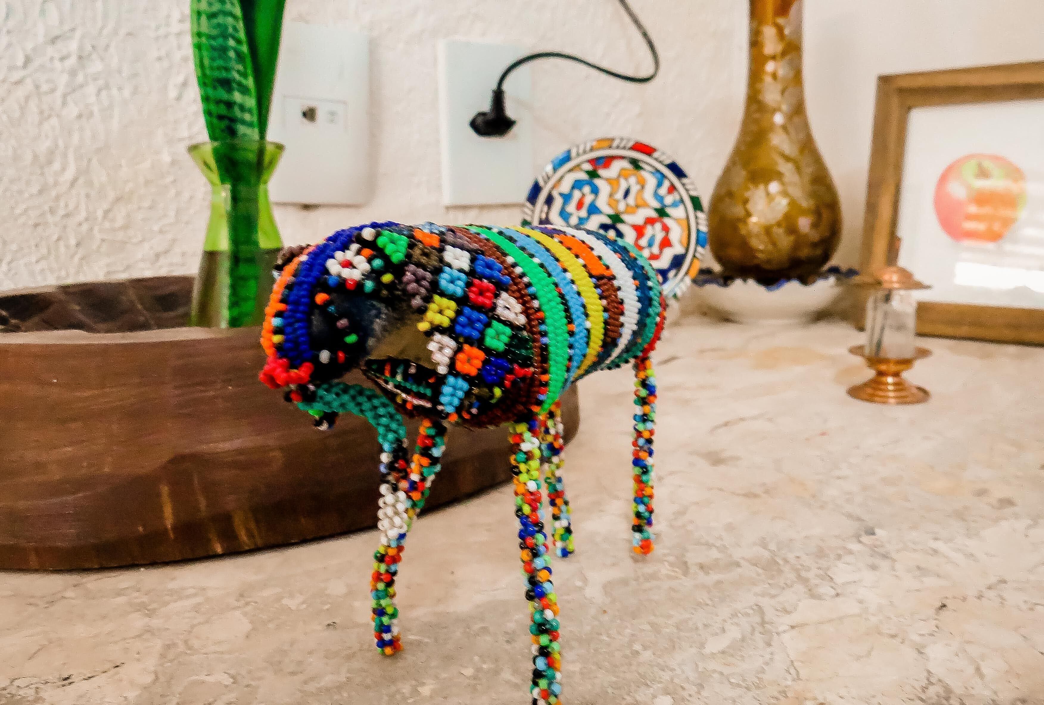 A beaded dog figurine on a marble floor with a vase and framed picture in the background.