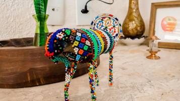 Una figurita de perro con cuentas sobre un piso de mármol, con un jarrón y un cuadro enmarcado al fondo.
