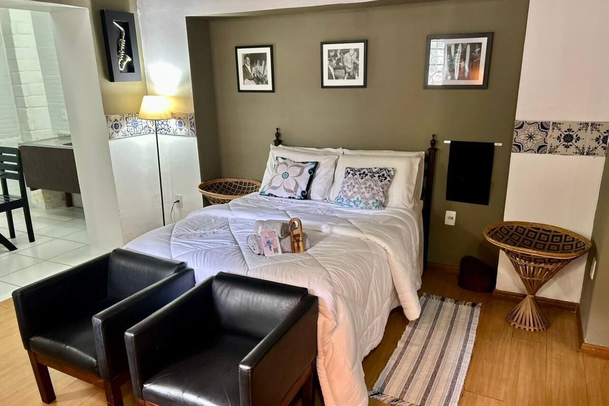 Une chambre à coucher comprenant un lit, deux chaises, une table de chevet et un haut-parleur fixé au mur.