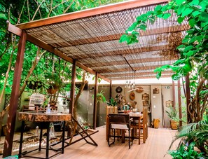 An indoor garden with a wooden table and chairs, surrounded by lush greenery and a bamboo roof structure. - Casa Perpetua hotel d charm (Manaus)