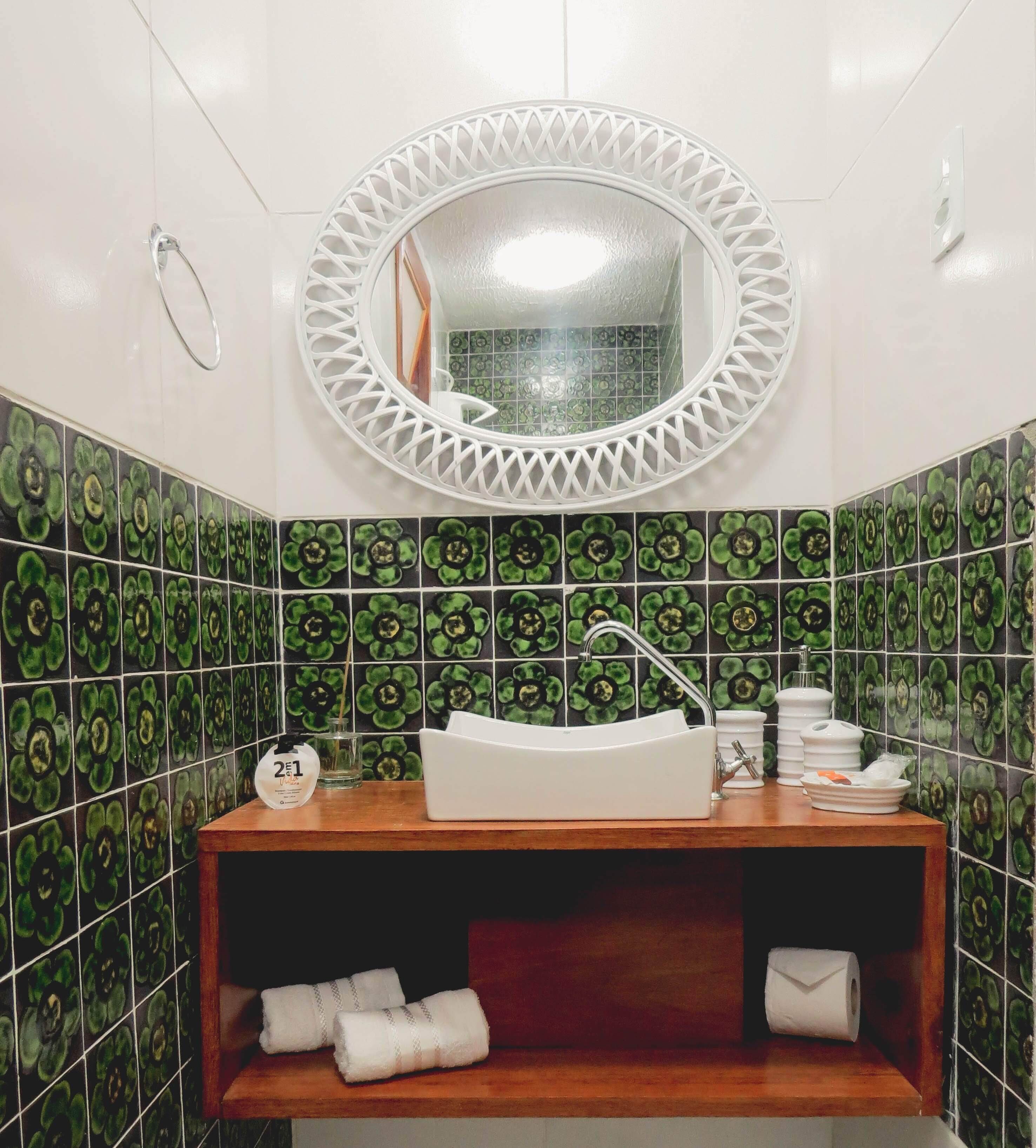 A bathroom with a white sink, a round mirror with a white frame, and green floral tiles on the walls.