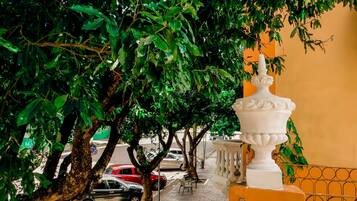 Un balcón con una urna decorativa blanca, una calle arbolada y coches estacionados.