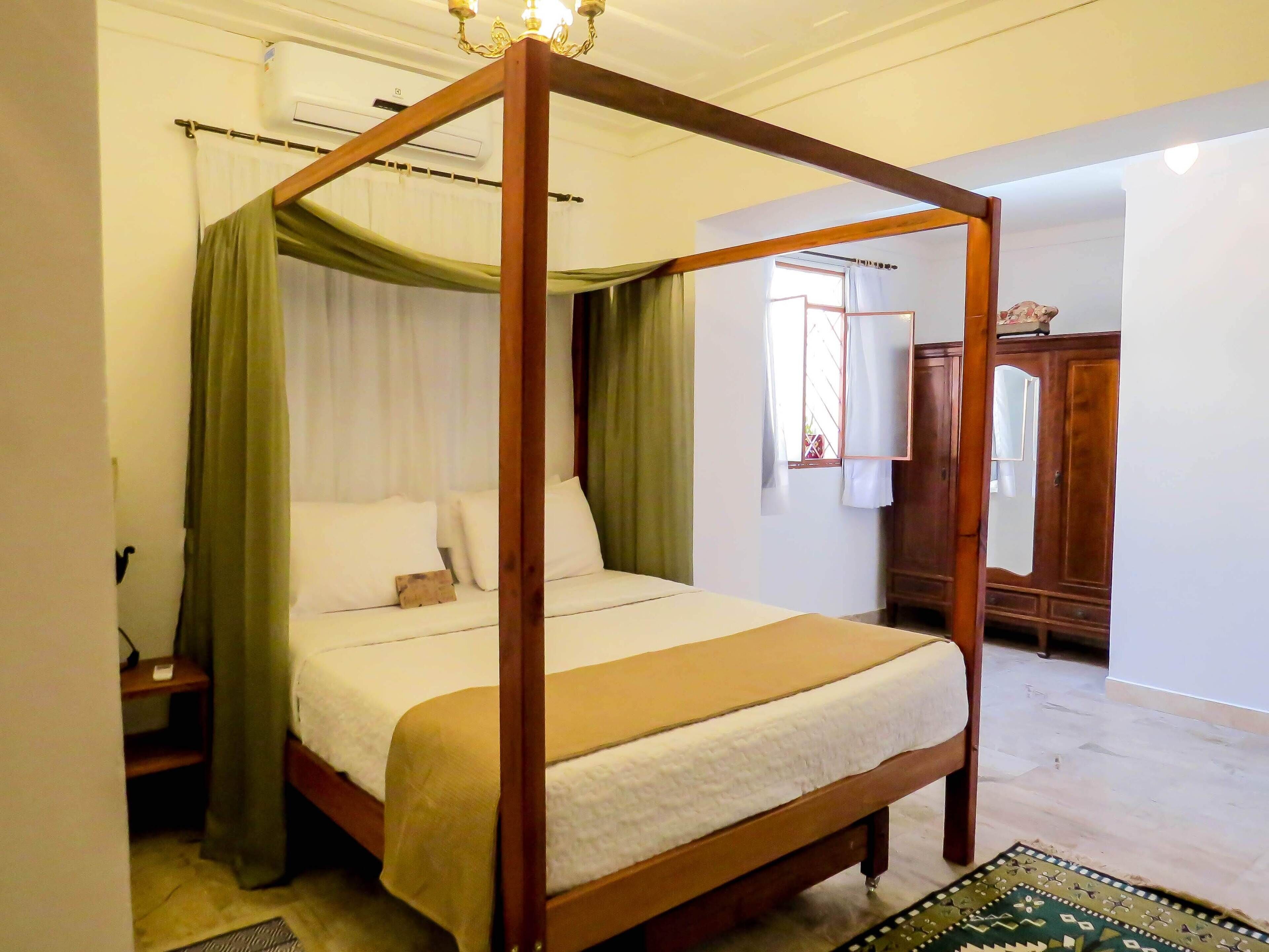 A four-poster bed with a wooden frame, white bedding, and green curtains.