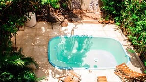 An outdoor swimming pool with a tiled deck, surrounded by potted plants and wooden lounge chairs.