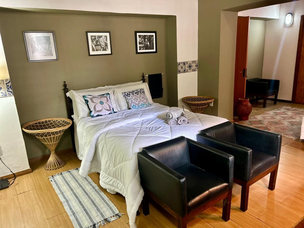 A bedroom with a bed, two chairs, a small table, a wall-mounted TV, and framed pictures.