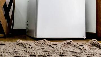 A white refrigerator in a room with a wooden floor and a knitted rug.