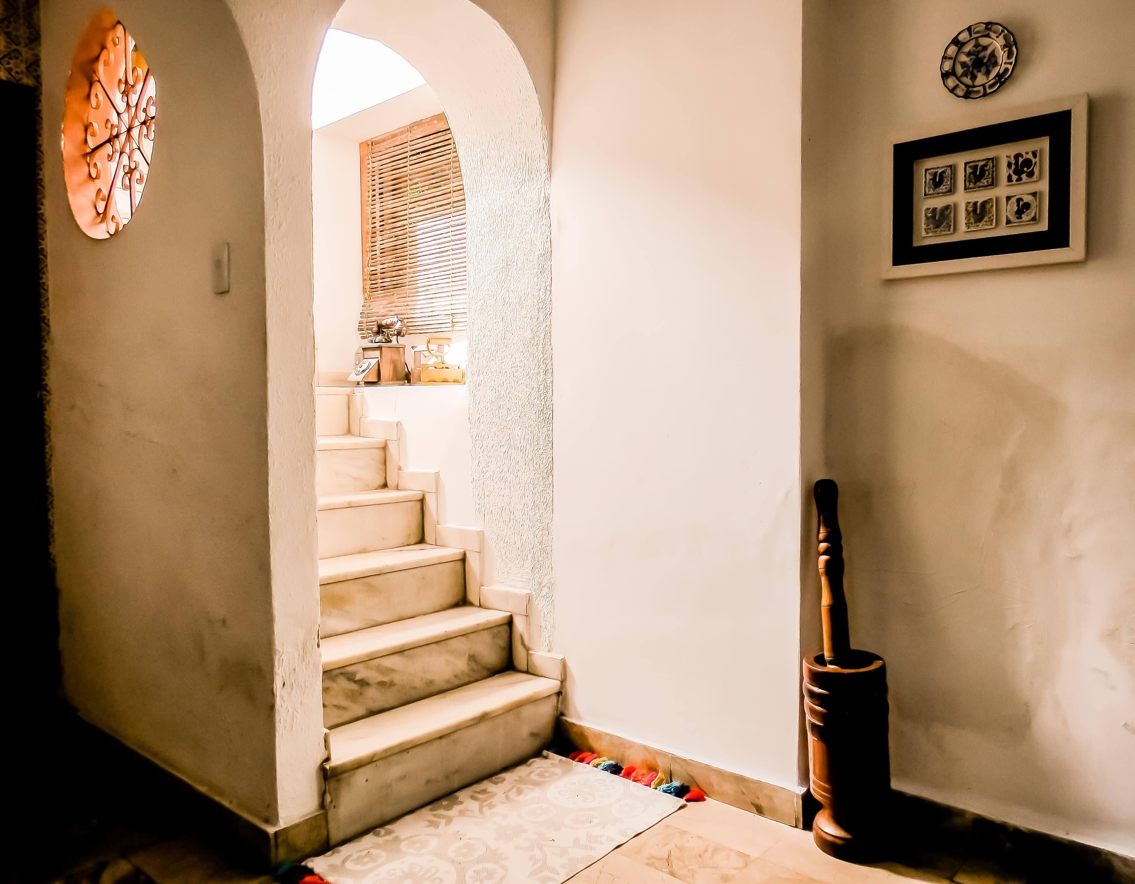 Una escalera que lleva a una habitación con ventana, un reloj en la pared y un cuadro enmarcado.