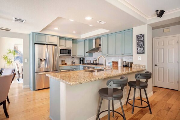 Una cocina moderna con armarios azul claro, electrodomésticos de acero inoxidable, encimera de granito y una zona con taburetes de bar.