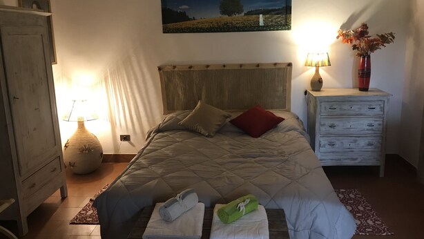 Quarto com cama, mesa de cabeceira, luminária, cômoda e um quadro na parede.