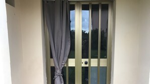 Uma porta com cortina amarrada na parte superior, uma lixeira de arame metálico à direita e um tapete de entrada em frente.