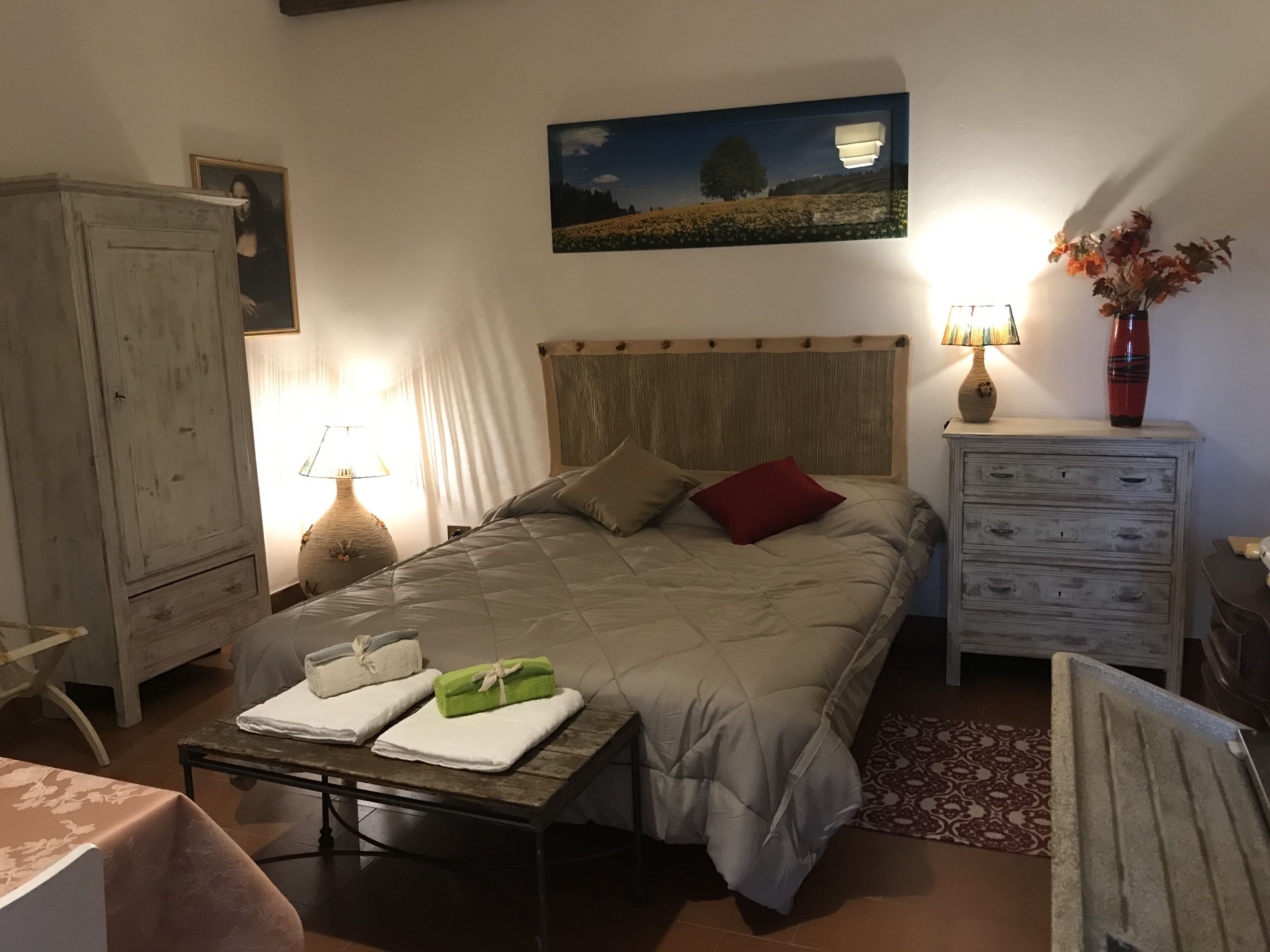 Una camera da letto con un letto, un comodino, una cassettiera, una lampada e un quadro appeso al muro.