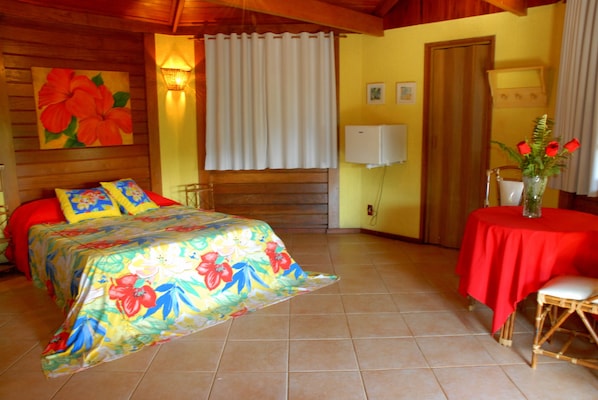 A room with a bed, a table with a red tablecloth, and a vase with flowers. - Pousada Vitorino (Angra dos Reis)