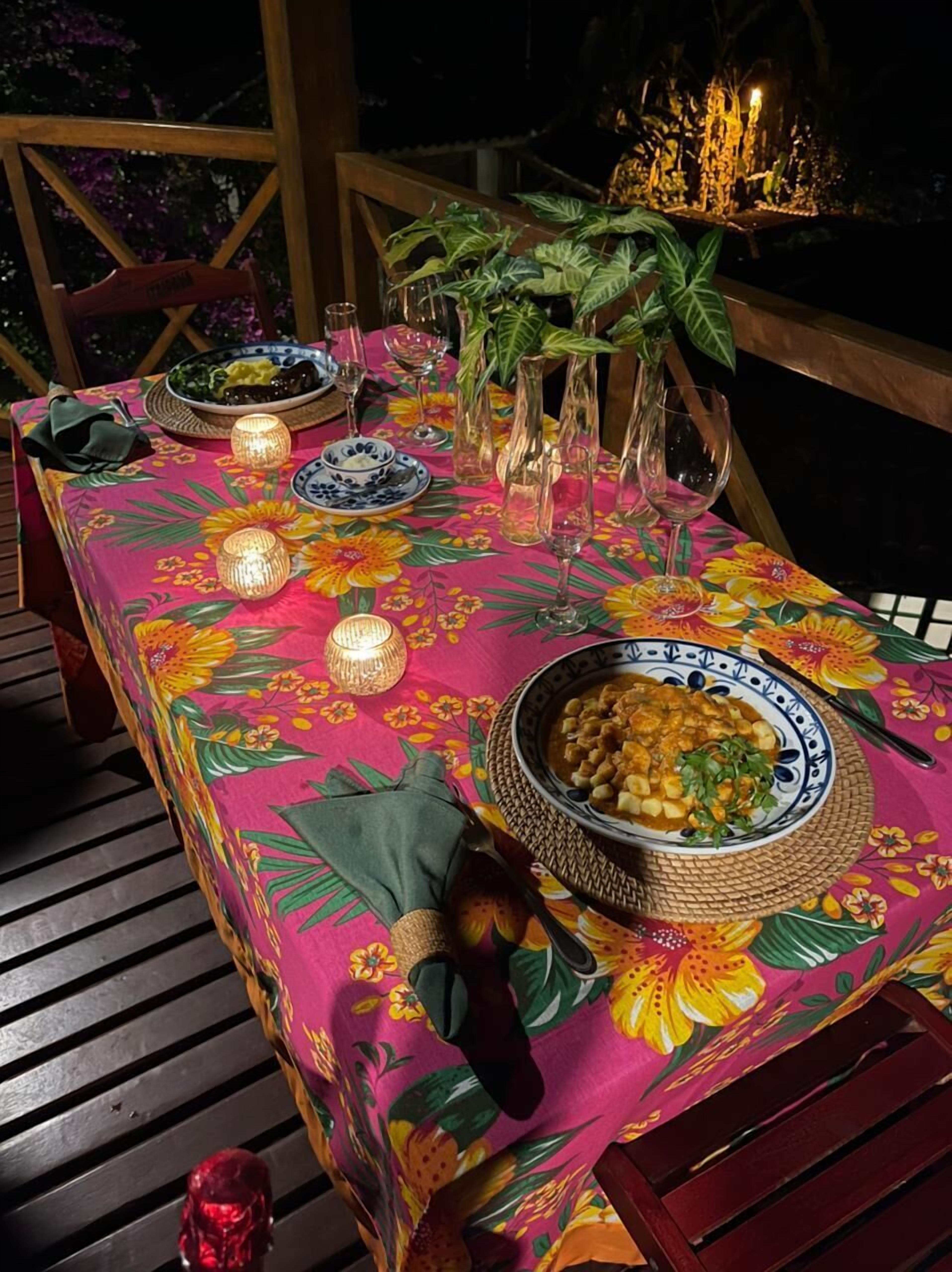 An outdoor dining table set with a floral tablecloth, lit candles, and various dishes.