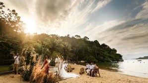 Ceremonia de boda en la playa con un altar de arena, invitados sentados sobre la arena y un telón de fondo de selva tropical y océano.